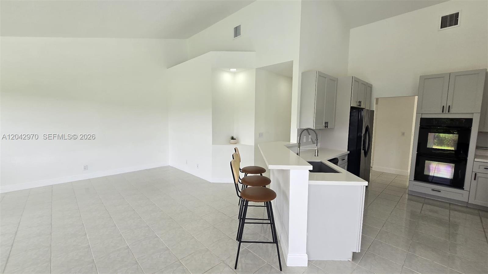 A kitchen with light gray cabinets, white countertops, and a breakfast bar with three stools — 10320 Guatemala St, Cooper City FL 33026, COOPER CITY, FL