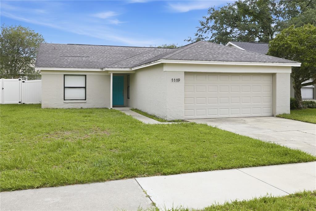 A single-story house with a beige stucco exterior, a gray shingled roof, and a blue door — 1119 COVINGTON STREET, OVIEDO, FL