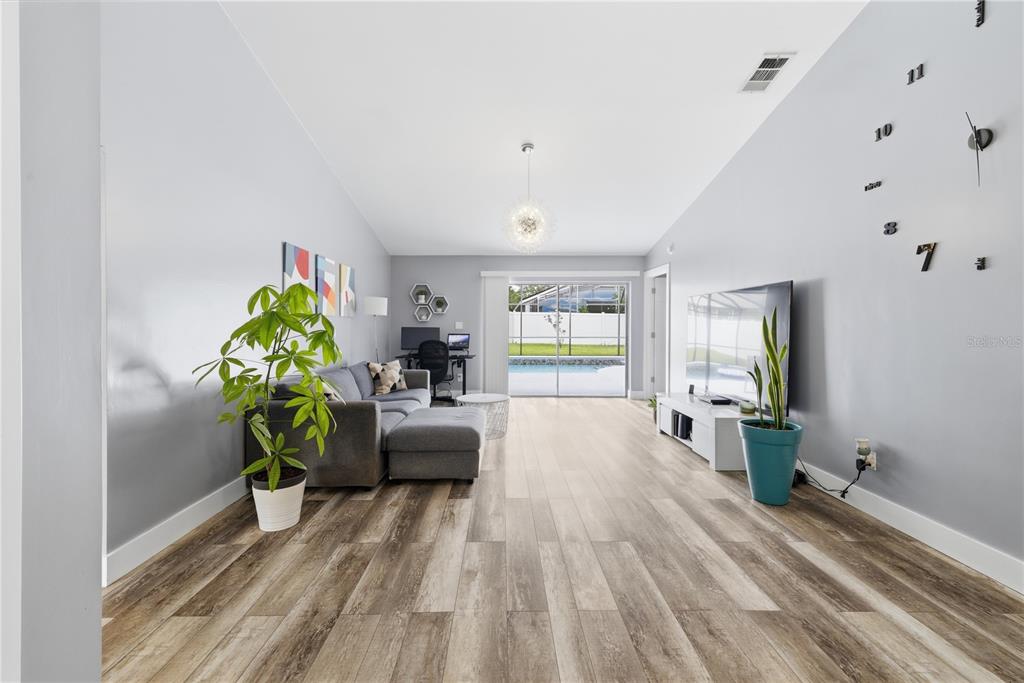 A living room with wood-look flooring, a gray sectional sofa, and a large wall clock — 1119 COVINGTON STREET, OVIEDO, FL