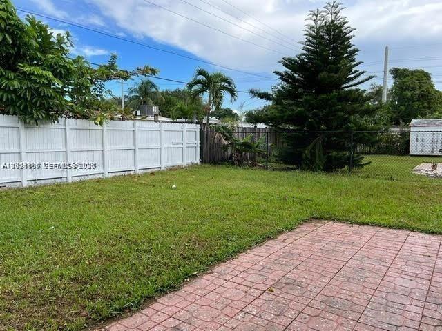 A grassy backyard features a white vinyl fence, a large pine tree, and brick pavers — 6431 Hayes St, Hollywood FL 33024, HOLLYWOOD, FL