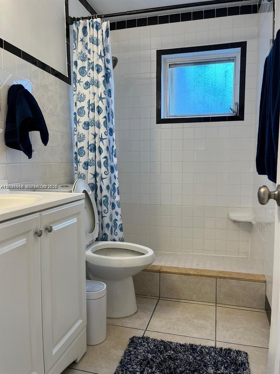 A bathroom features a white vanity, a toilet, and a tiled walk-in shower with curtains — 6431 Hayes St, Hollywood FL 33024, HOLLYWOOD, FL
