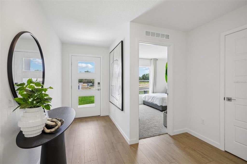 A bright entryway features light wood flooring, a modern front door, and a side bedroom — 231 SKYFIELD COURT, LADY LAKE, FL