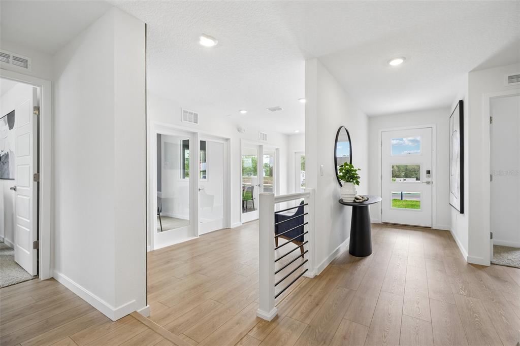 A bright entryway features light wood flooring, a white front door, and a modern staircase — 231 SKYFIELD COURT, LADY LAKE, FL