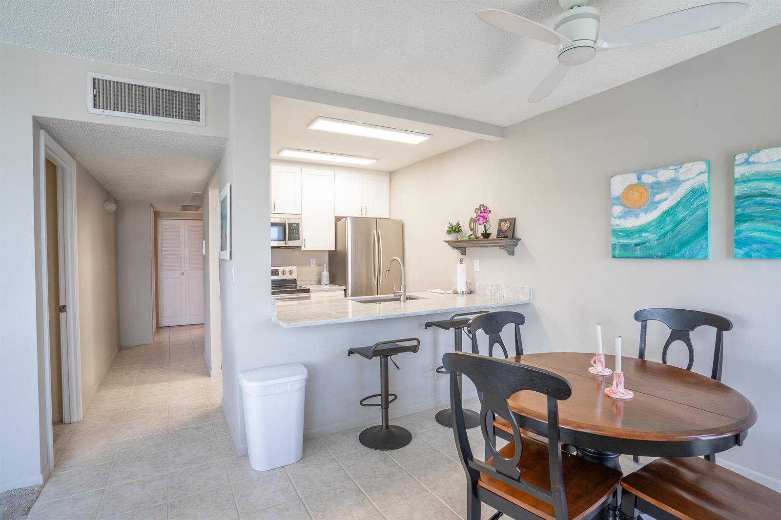 A kitchen with white cabinets and granite countertops opens to a dining area with a table — 250 NE 20th Street # 4190, Boca Raton FL 33431, BOCA RATON, FL