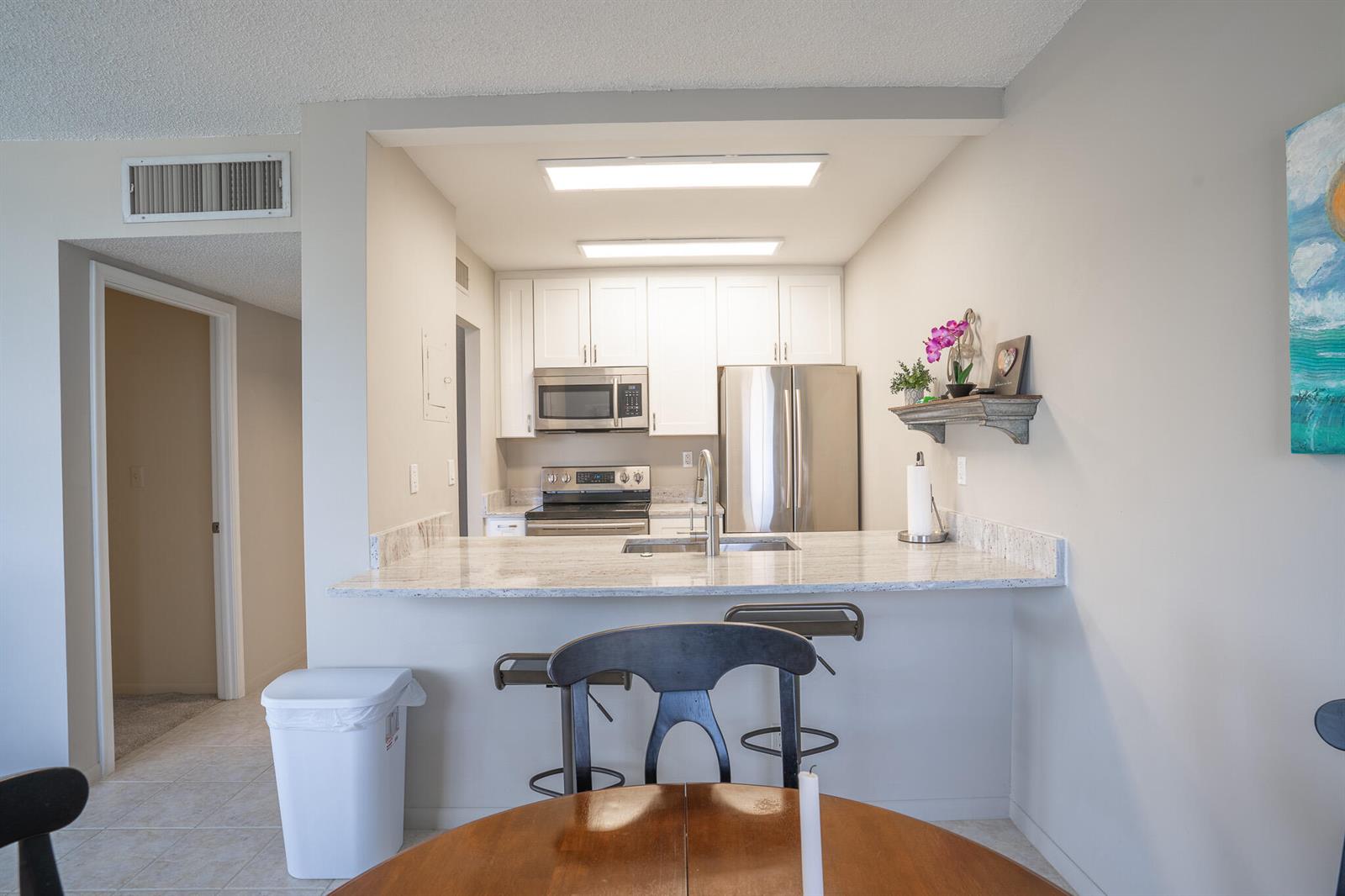 A kitchen with white cabinets, stainless steel appliances, and a granite breakfast bar — 250 NE 20th Street # 4190, Boca Raton FL 33431, BOCA RATON, FL