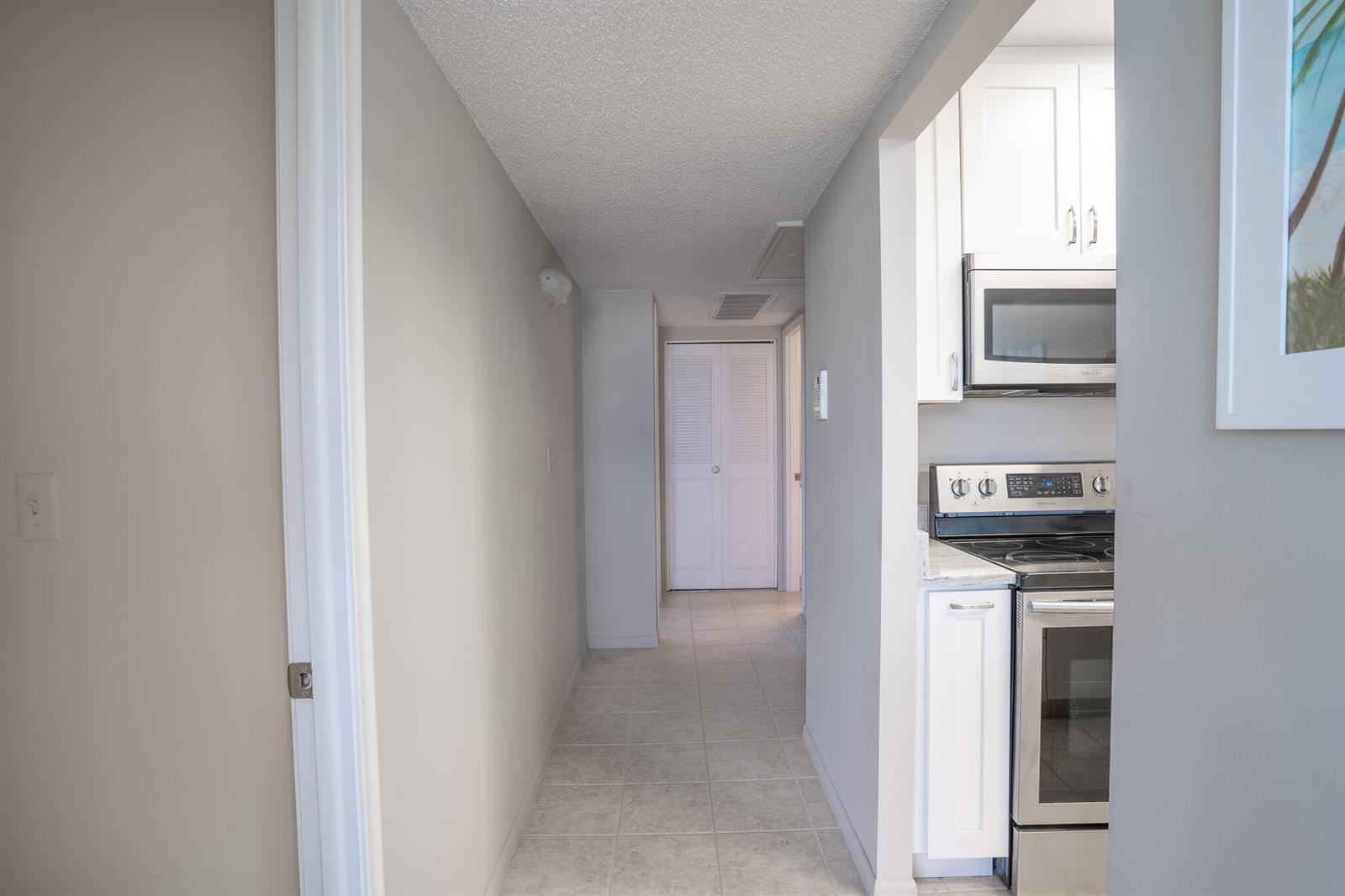 A hallway with tiled flooring leads toward a white door, adjacent to a compact kitchen — 250 NE 20th Street # 4190, Boca Raton FL 33431, BOCA RATON, FL