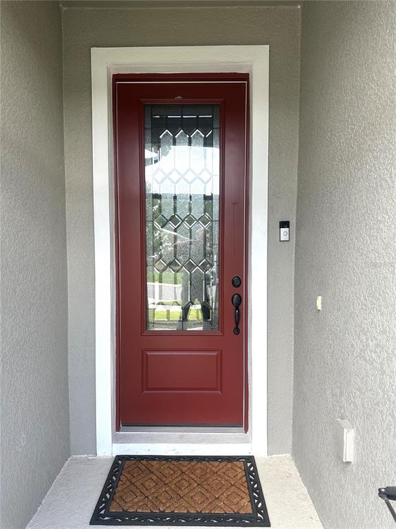 A red front door with a decorative glass insert sits in a gray stucco entryway — 5726 ARLINGTON RIVER DRIVE, LAKELAND, FL