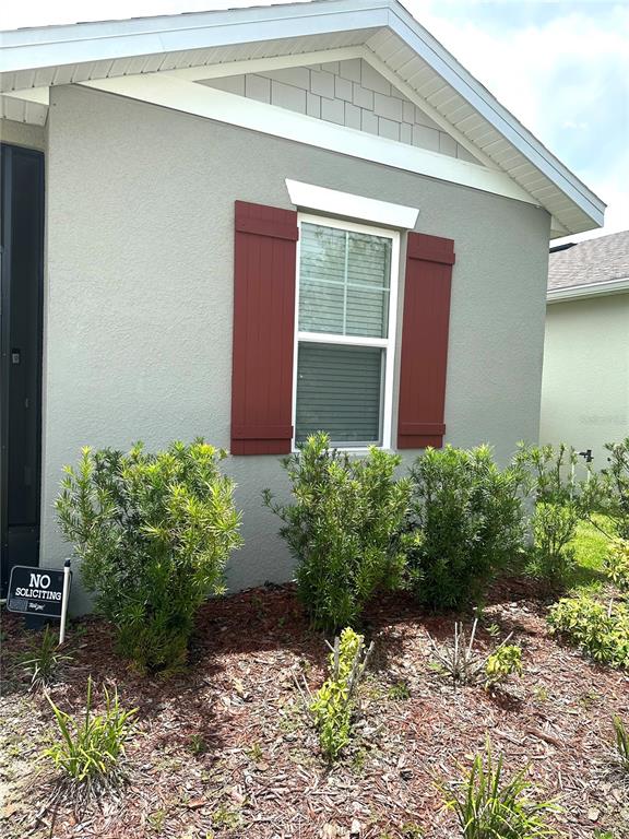 A gray house exterior features a window with red shutters and a small garden bed — 5726 ARLINGTON RIVER DRIVE, LAKELAND, FL