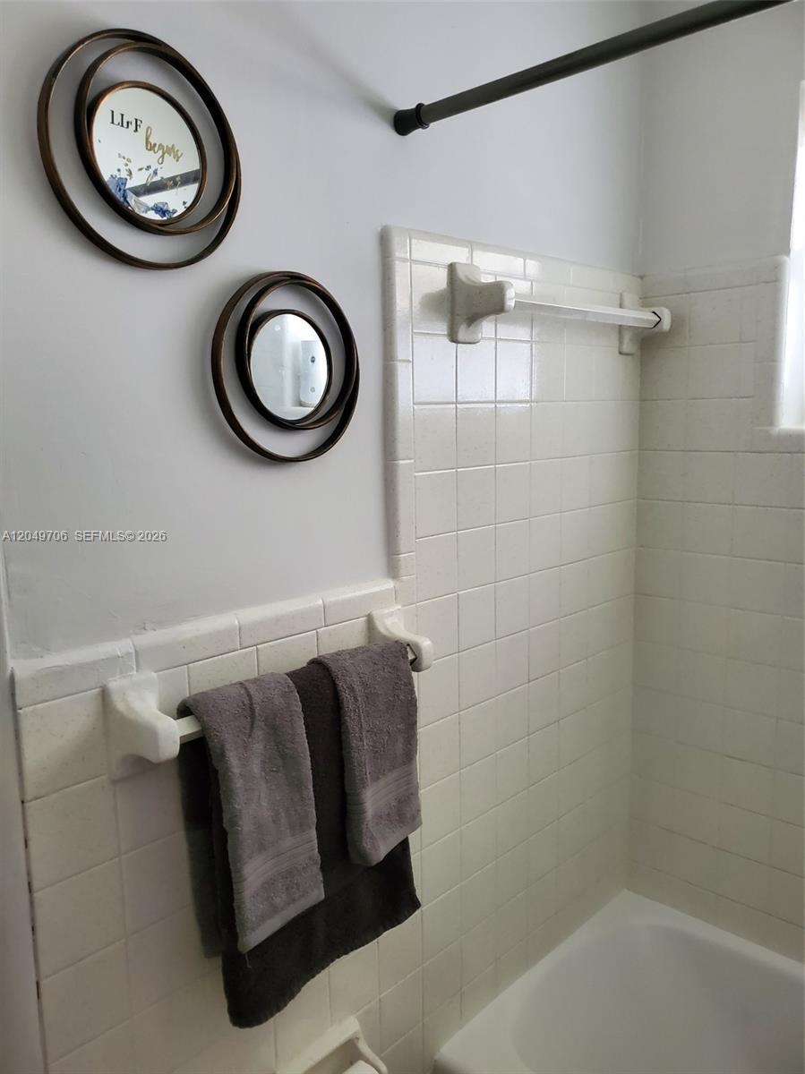 A bathroom features a white tiled shower surround, two towel bars, and circular wall decor — 804 NW 8th St, Dania Beach FL 33004, DANIA BEACH, FL