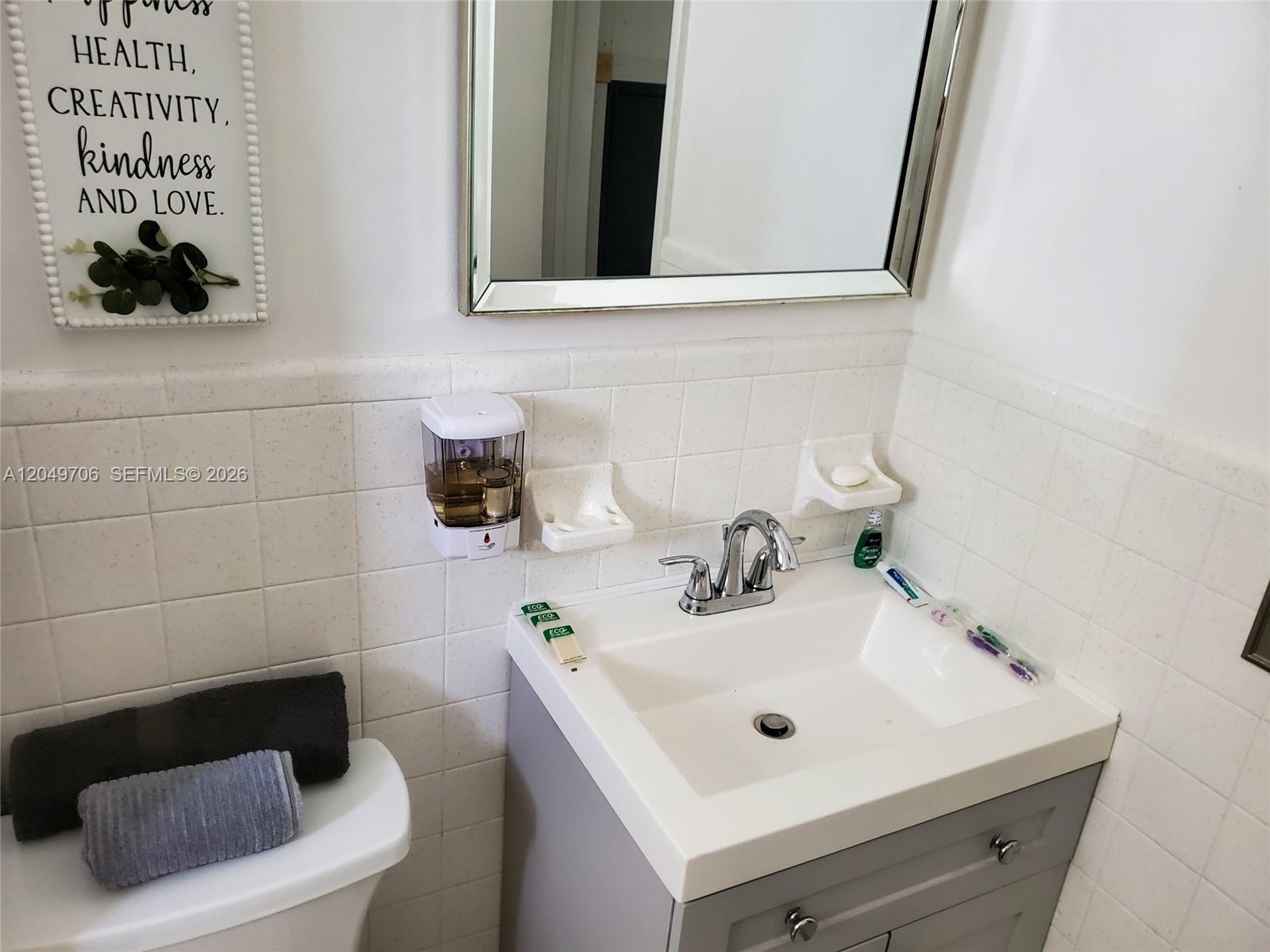 A bathroom features a white sink, gray vanity, wall-mounted soap dispenser, and tiled walls — 804 NW 8th St, Dania Beach FL 33004, DANIA BEACH, FL