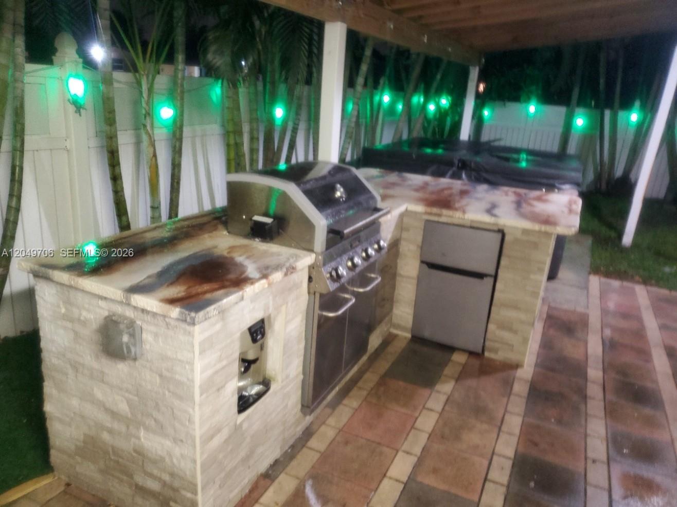 An outdoor kitchen features a stainless steel grill, a small refrigerator, and stone-tiled counters — 804 NW 8th St, Dania Beach FL 33004, DANIA BEACH, FL