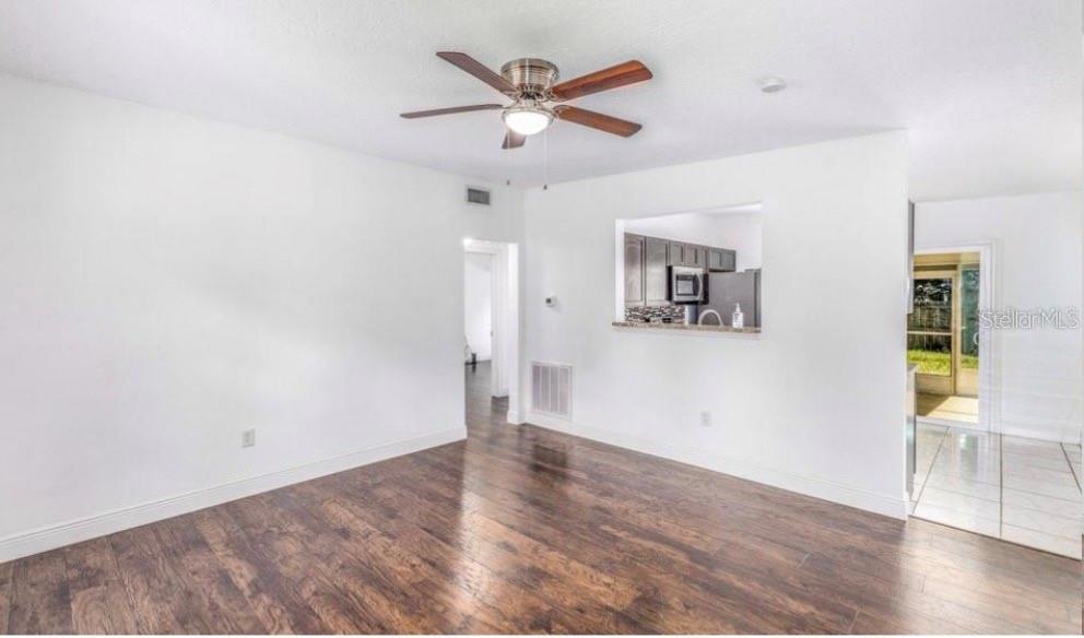 An empty living room features dark wood-look flooring, a ceiling fan, and a kitchen pass-through — 1625 QUEENSWAY ROAD, ORLANDO, FL