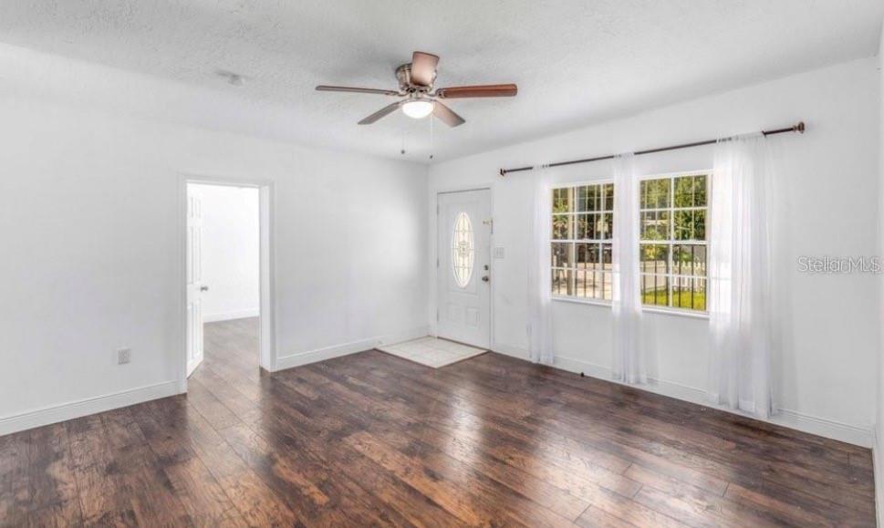 A bright living room features white walls, dark wood-look flooring, a ceiling fan, and windows — 1625 QUEENSWAY ROAD, ORLANDO, FL