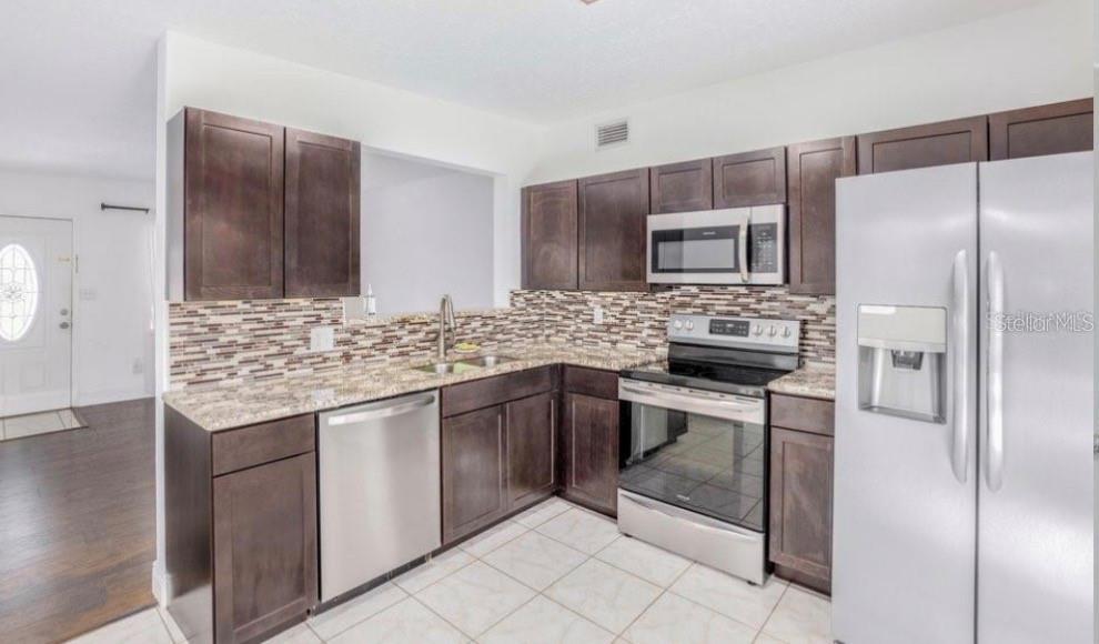 A kitchen with dark wood cabinets, granite countertops, stainless steel appliances, and a tiled floor — 1625 QUEENSWAY ROAD, ORLANDO, FL
