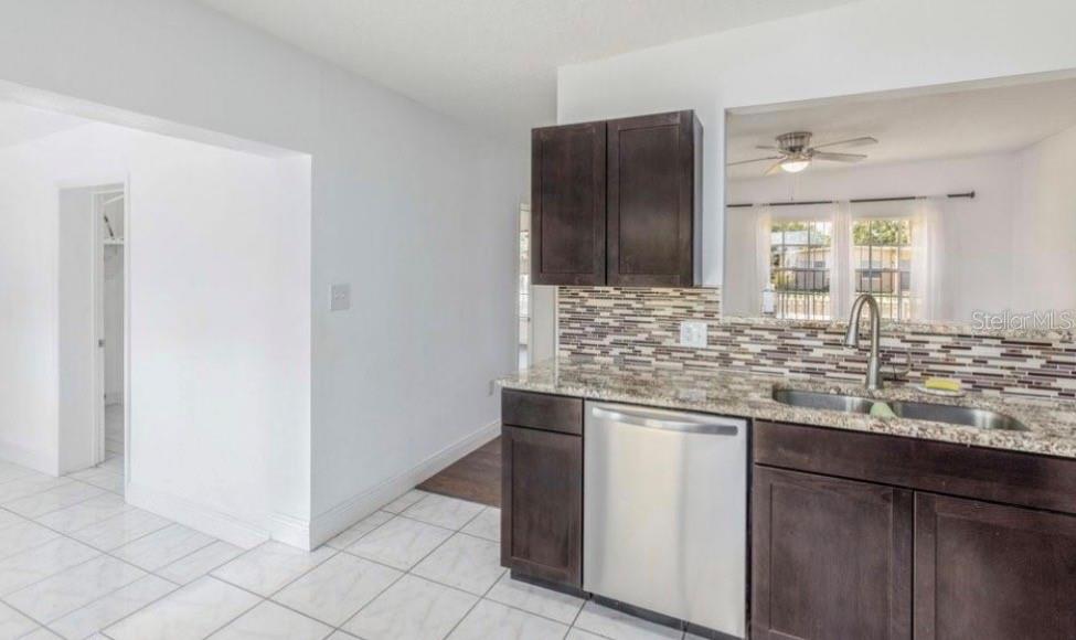 A kitchen features dark wood cabinets, granite countertops, a stainless steel dishwasher, and tiled flooring — 1625 QUEENSWAY ROAD, ORLANDO, FL