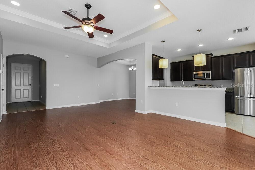 An open-concept living area features wood-look flooring, a tray ceiling, and an adjacent kitchen — 3911 CONSTANTINE LOOP, WESLEY CHAPEL, FL