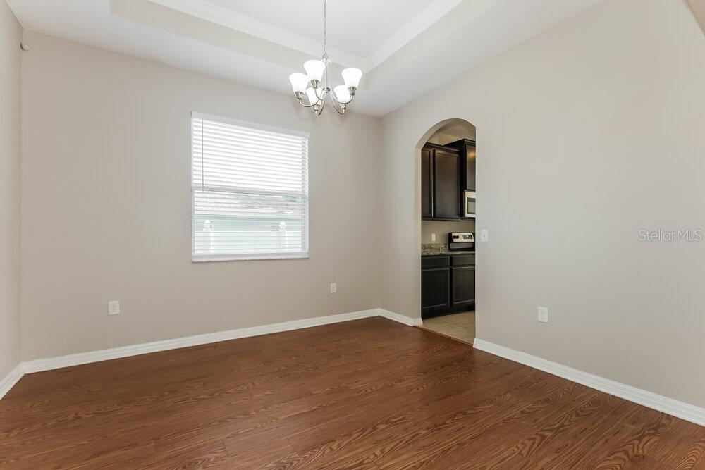 An empty dining room features wood-look flooring, a chandelier, and an arched doorway to the kitchen — 3911 CONSTANTINE LOOP, WESLEY CHAPEL, FL