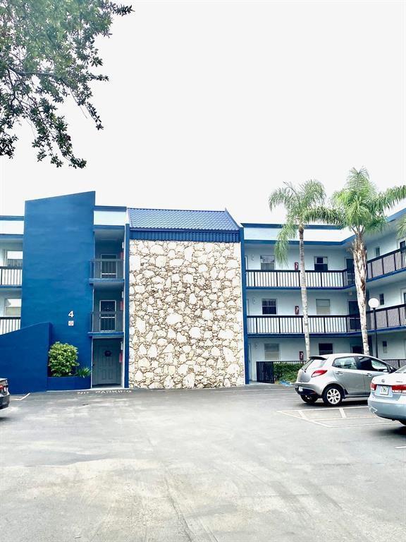 An exterior view of a blue apartment building with a stone facade and palm trees — 3130 Holiday Springs Boulevard # 104, Margate FL 33063, MARGATE, FL