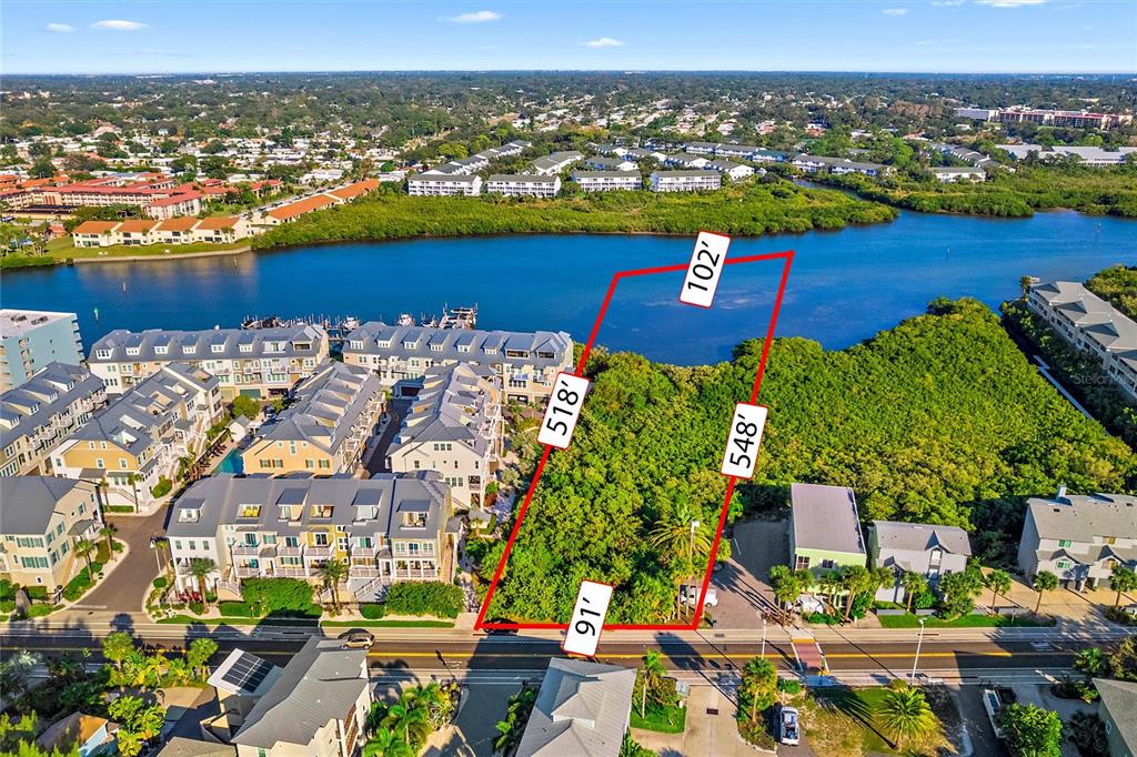 This aerial view shows a vacant, vegetated lot outlined in red along a waterfront — 19901 GULF BLVD, INDIAN SHORES, FL