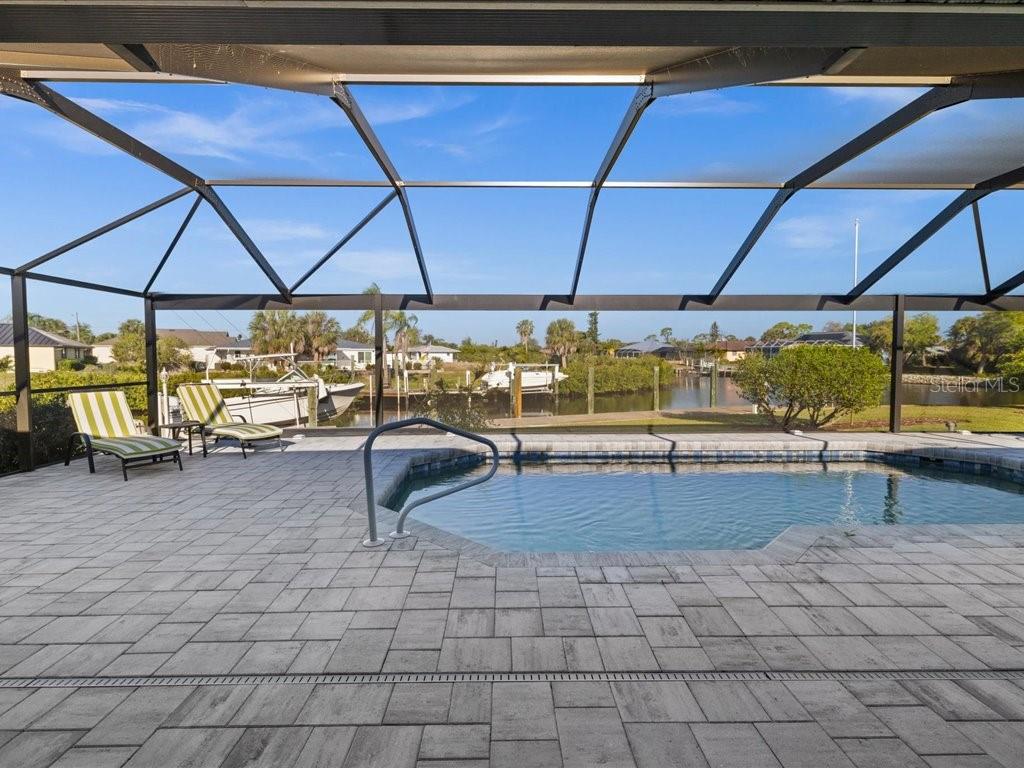 A screened-in patio features a swimming pool, stone pavers, and a view of a canal — 18350 VAN NUYS CIRCLE, PORT CHARLOTTE, FL