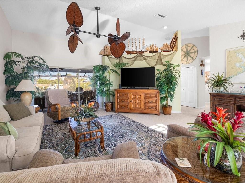 A living room features a vaulted ceiling, tropical decor, a large area rug, and furniture — 18350 VAN NUYS CIRCLE, PORT CHARLOTTE, FL