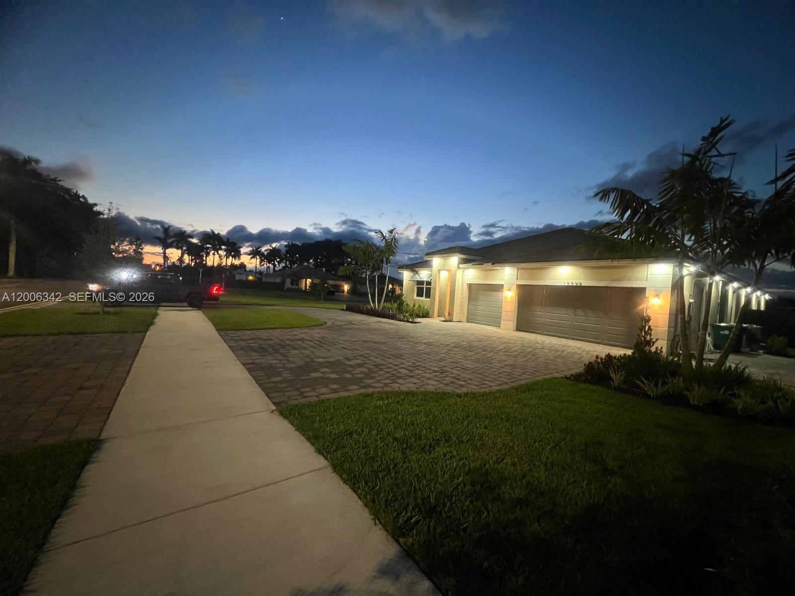 A paved driveway leads to a house with a three-car garage at twilight — 17775 SW 296th St, Homestead FL 33030, HOMESTEAD, FL