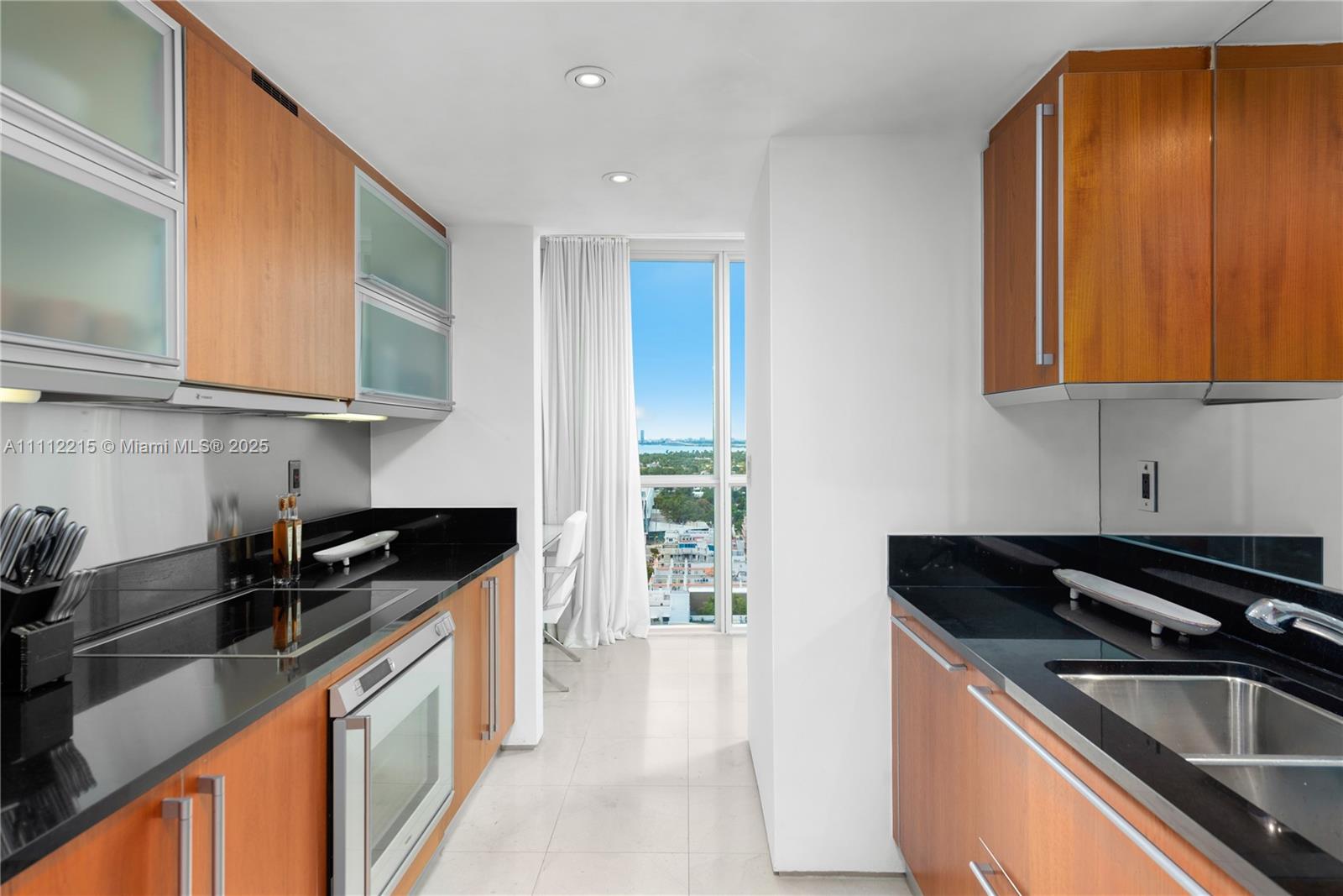 A galley kitchen features wood cabinets, black countertops, and a window with a city view — 101 20th St # 2401, Miami Beach FL 33139, MIAMI BEACH, FL