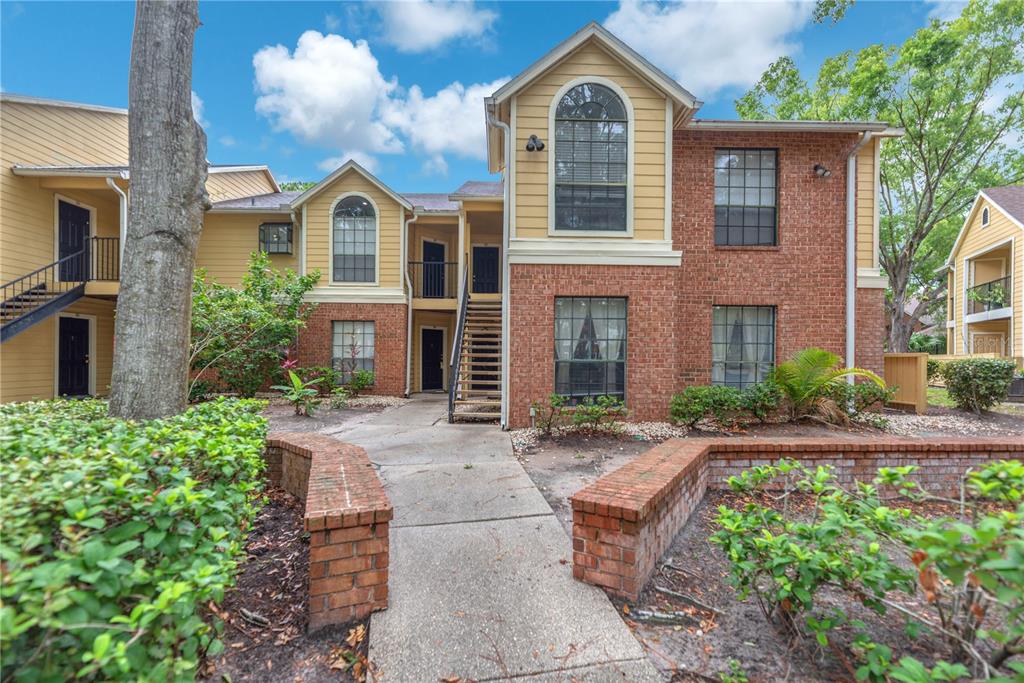 A two-story apartment building with brick and yellow siding features an exterior staircase and landscaping — 8609 MALLARD RESERVE DRIVE UNIT 203, TAMPA, FL