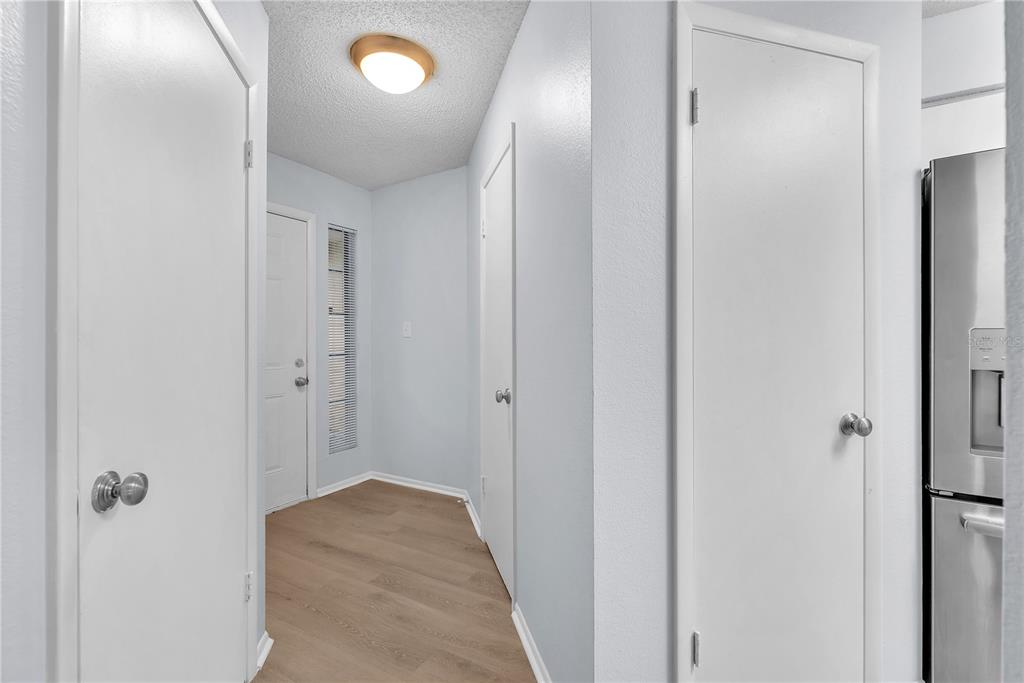 A hallway with light wood flooring, white doors, and a ceiling light fixture — 8609 MALLARD RESERVE DRIVE UNIT 203, TAMPA, FL