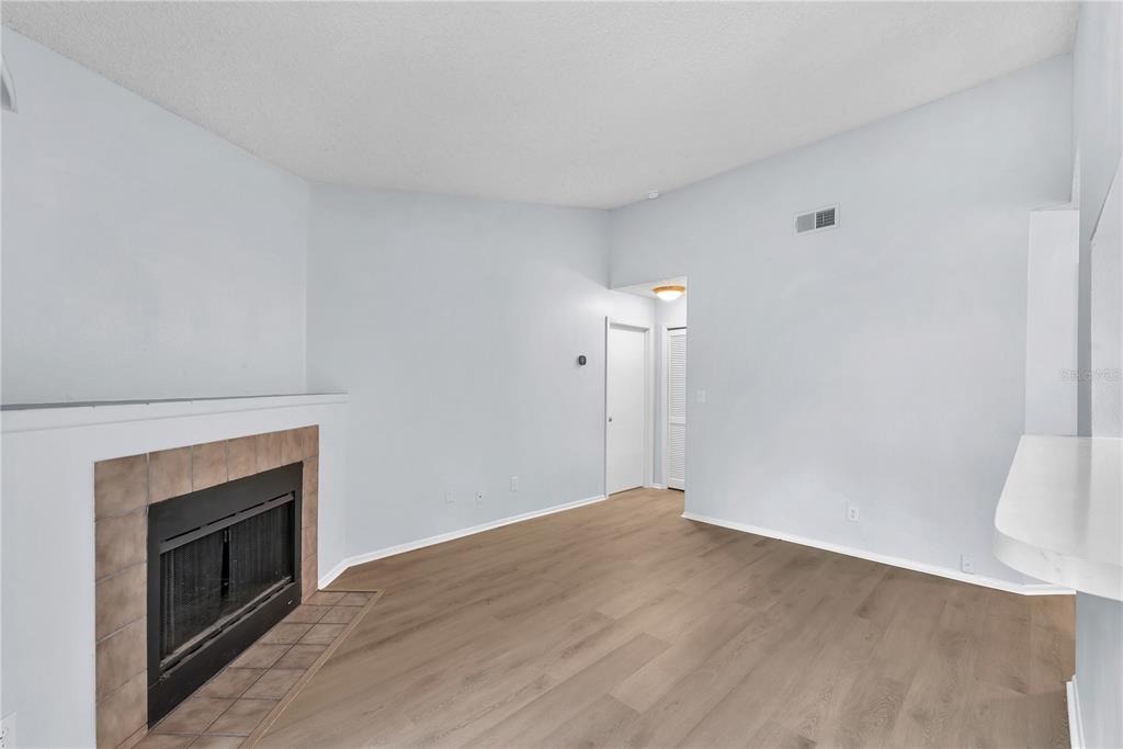 An empty living room features light wood-look flooring, a fireplace with brown tiles, and white walls — 8609 MALLARD RESERVE DRIVE UNIT 203, TAMPA, FL