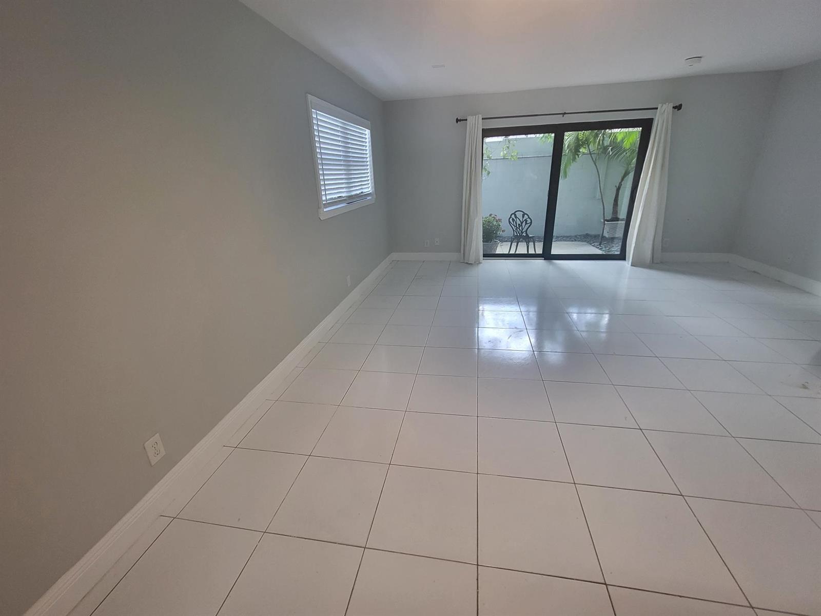 An empty room with light gray walls, white tile flooring, and a sliding glass door — 4135 NE 21st Terrace, Lighthouse Point FL 33064, LIGHTHOUSE POINT, FL