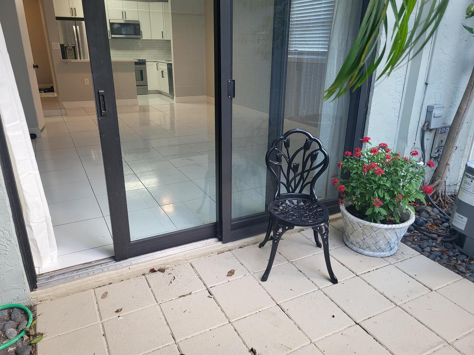 A patio with a black metal chair and a potted plant sits outside a sliding door — 4135 NE 21st Terrace, Lighthouse Point FL 33064, LIGHTHOUSE POINT, FL
