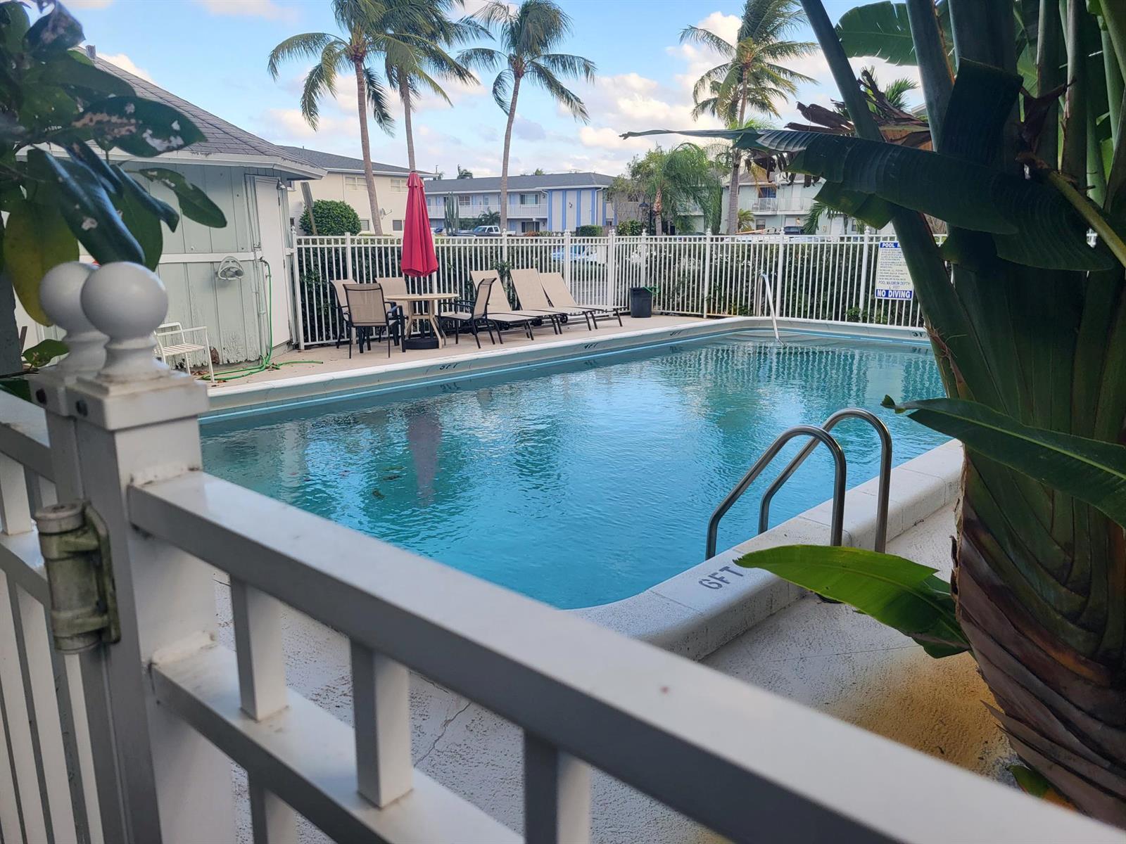 A swimming pool with lounge chairs and a patio table sits behind a white fence — 4135 NE 21st Terrace, Lighthouse Point FL 33064, LIGHTHOUSE POINT, FL