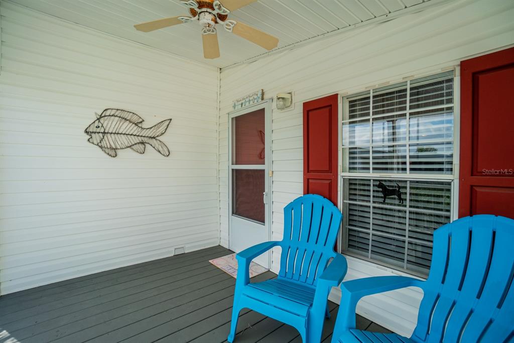 A covered porch features white siding, a ceiling fan, two blue chairs, and red shutters — 10303 BURNT STORE ROAD UNIT 203, PUNTA GORDA, FL