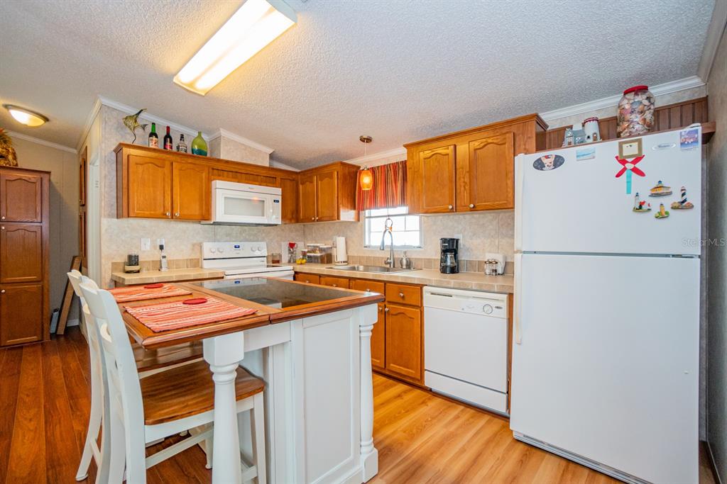 A kitchen features wooden cabinets, white appliances, a center island, and light wood flooring — 10303 BURNT STORE ROAD UNIT 203, PUNTA GORDA, FL