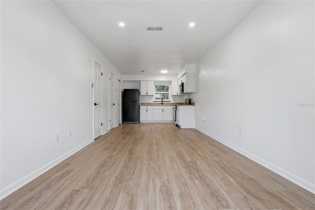 A bright kitchen and living area features white cabinets, stainless steel appliances, and wood-look flooring — 3108 SW 24TH DRIVE, GAINESVILLE, FL
