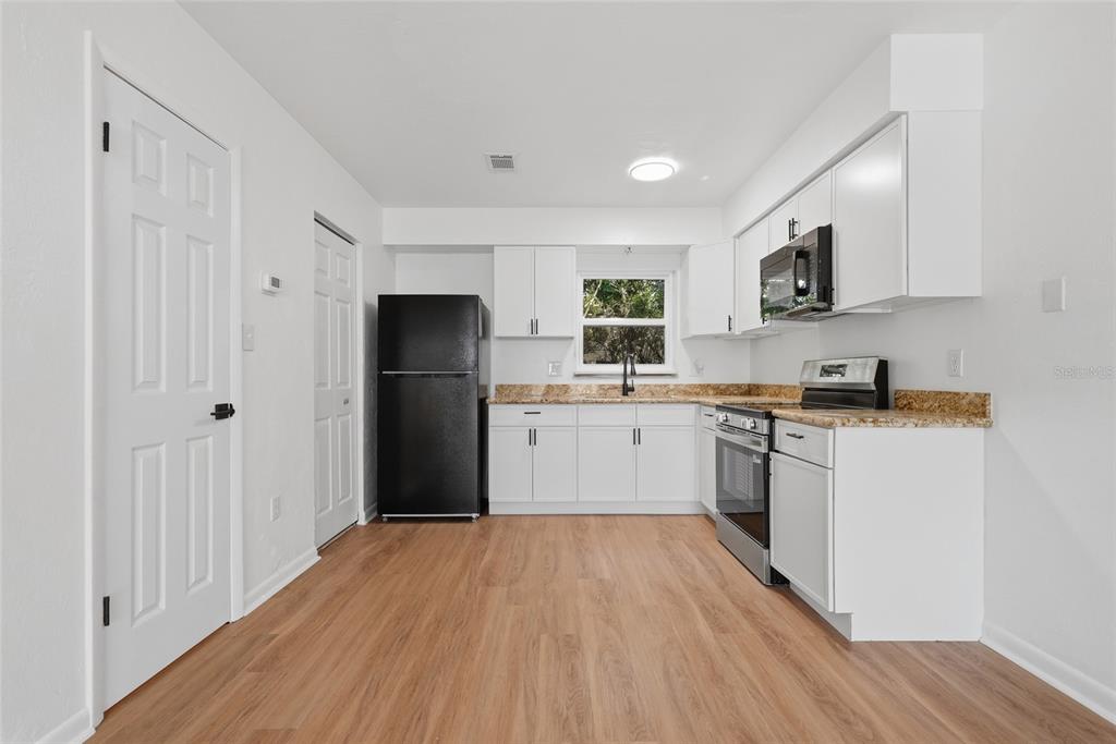 A kitchen with white cabinets, black appliances, granite countertops, and light wood-look flooring — 3108 SW 24TH DRIVE, GAINESVILLE, FL