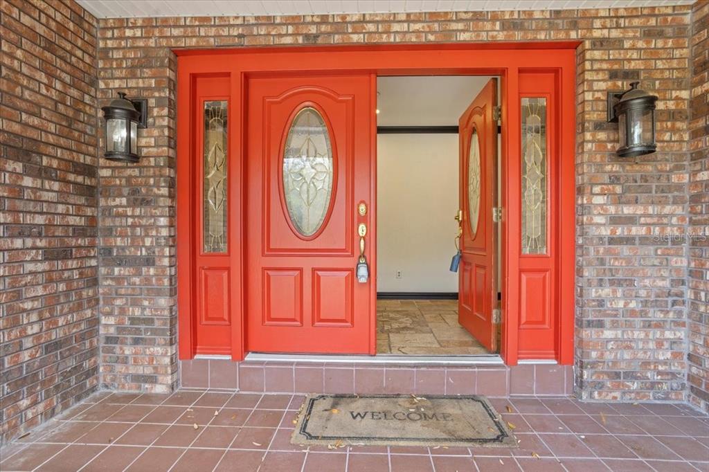 A bright orange double front door with glass inserts is set in a brick wall — 201 S SWEETWATER COVE BOULEVARD, LONGWOOD, FL