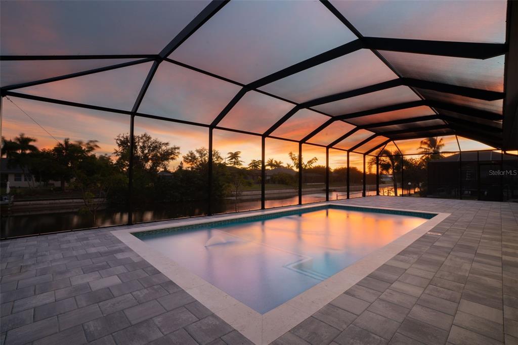 A screened-in swimming pool patio overlooks a canal at sunset — 836 SW 36TH TERRACE, CAPE CORAL, FL