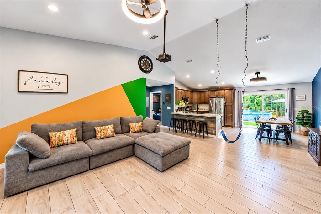 A living room with a gray sectional, a swing, and an open kitchen with island seating — 126 LOCUST RADIAL, OCALA, FL