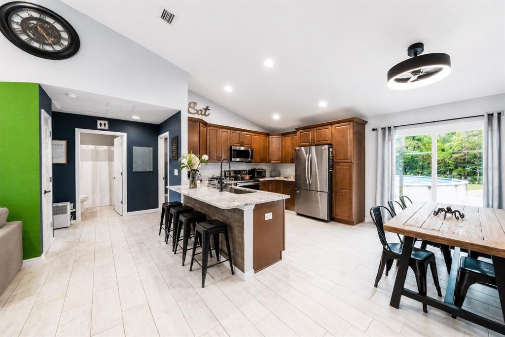 A kitchen features wood cabinets, a granite-topped island with bar stools, and tile flooring — 126 LOCUST RADIAL, OCALA, FL