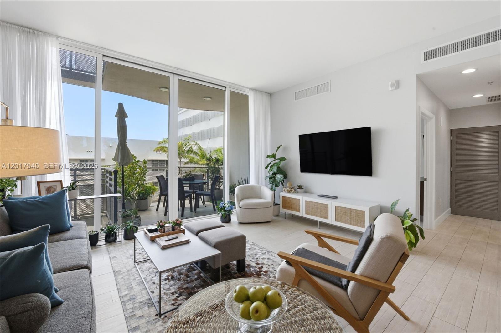 A bright living room features a television, modern furniture, and a balcony with outdoor seating — 2100 Park Ave # 302, Miami Beach FL 33139, MIAMI BEACH, FL