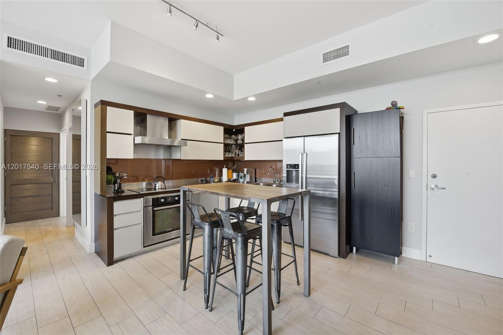 A modern kitchen features stainless steel appliances, white and dark wood cabinetry, and a table — 2100 Park Ave # 302, Miami Beach FL 33139, MIAMI BEACH, FL