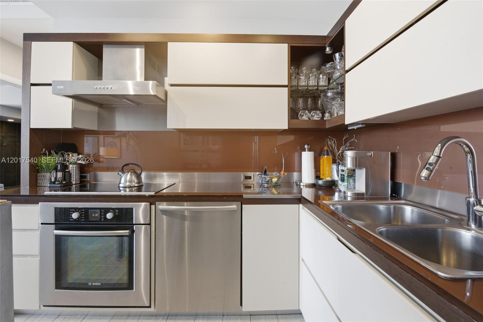 A modern kitchen features stainless steel appliances, white cabinetry, and a brown glass backsplash — 2100 Park Ave # 302, Miami Beach FL 33139, MIAMI BEACH, FL