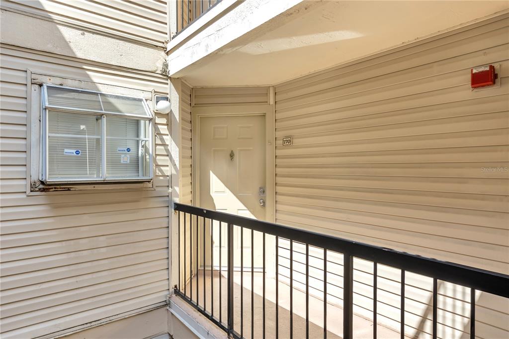 An exterior view of an apartment entrance with beige siding and a black metal railing — 1964 LAKE ATRIUMS CIRCLE UNIT 170, ORLANDO, FL