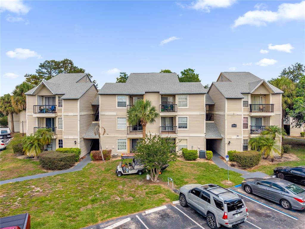 A three-story apartment building with beige siding, balconies, and a parking lot in front — 1964 LAKE ATRIUMS CIRCLE UNIT 170, ORLANDO, FL