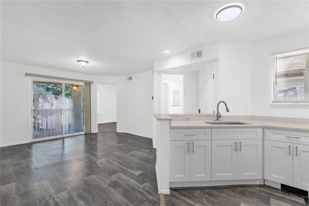 A kitchen with white cabinets and a sink overlooks a living area with wood flooring — 1964 LAKE ATRIUMS CIRCLE UNIT 170, ORLANDO, FL