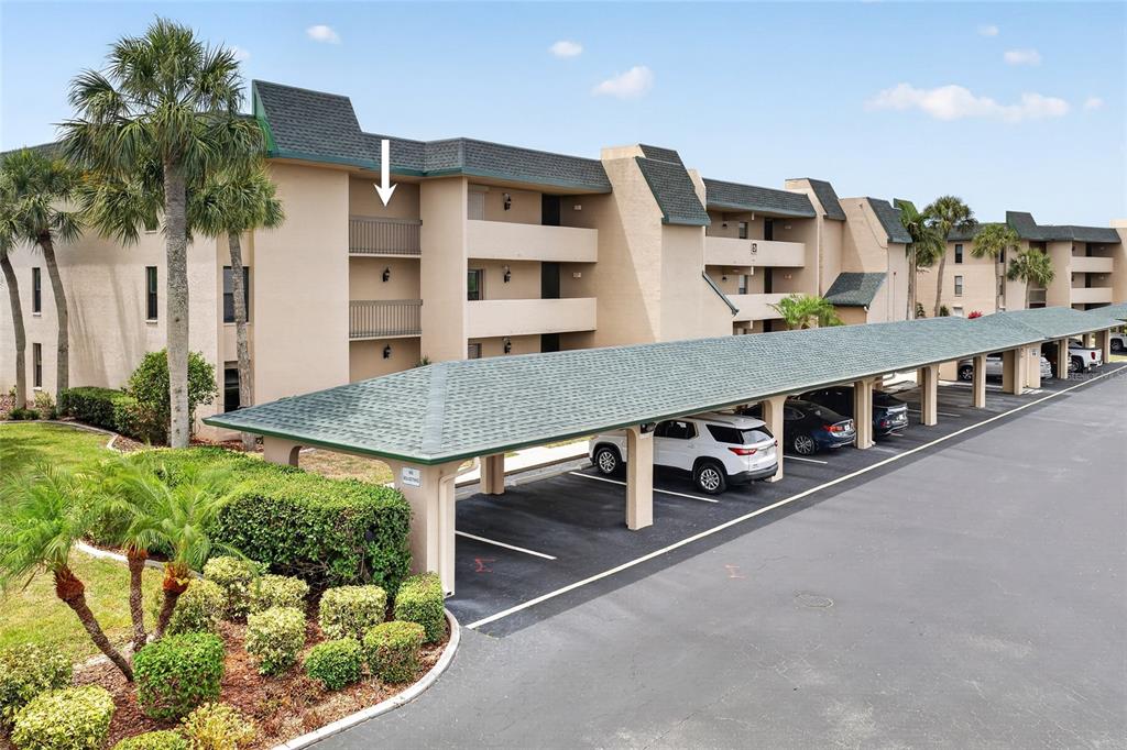 An exterior view of a multi-story apartment building with covered parking spaces in the foreground — 601 SHREVE STREET UNIT 51C, PUNTA GORDA, FL