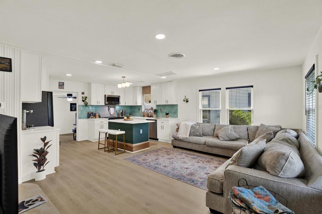 An open-concept living room and kitchen featuring white cabinets, a teal island, and gray furniture — 4828 6TH AVENUE S, ST PETERSBURG, FL