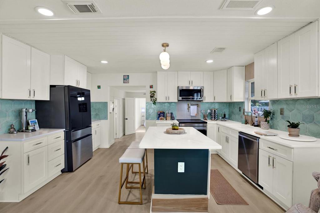 A kitchen features white cabinetry, a central island with seating, and a teal hexagonal backsplash — 4828 6TH AVENUE S, ST PETERSBURG, FL